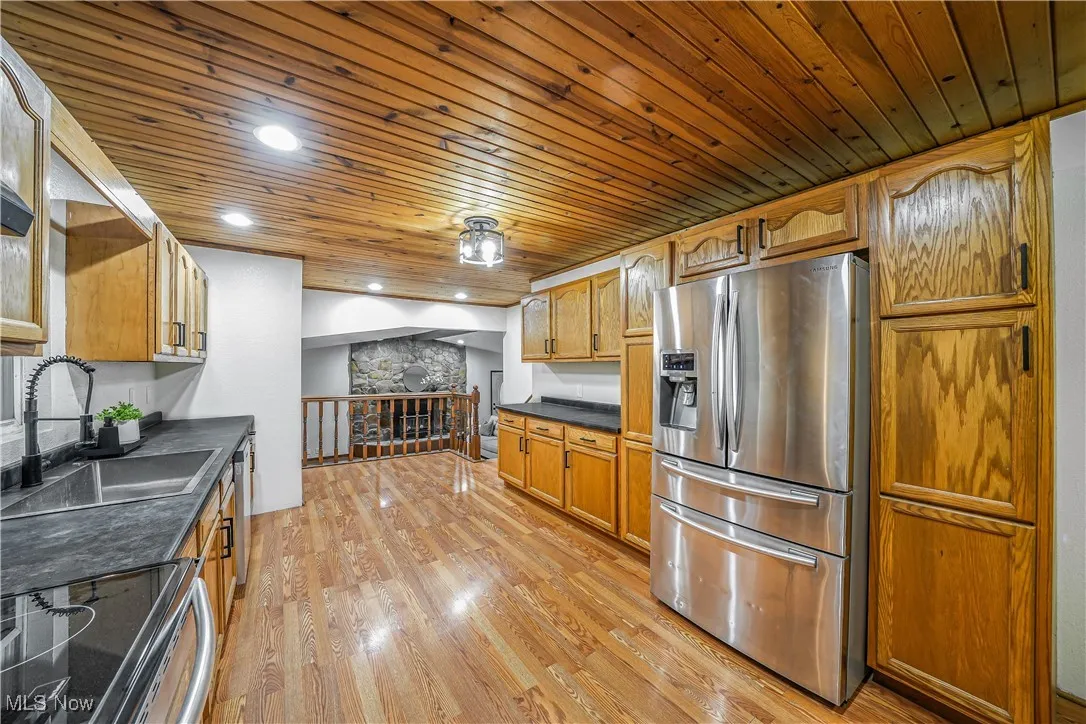 Kitchen featuring stainless steel appliances, dark countertops, wooden ceiling, light wood-type flooring, and brown cabinets