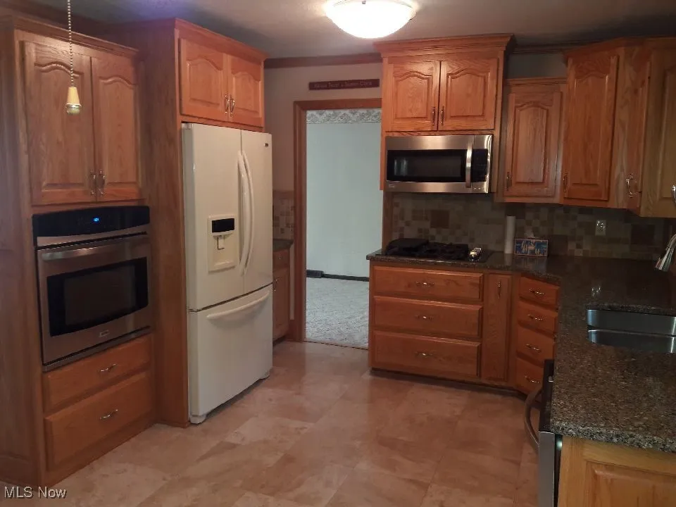 Kitchen with stainless steel appliances, backsplash, dark stone counters, and brown cabinets