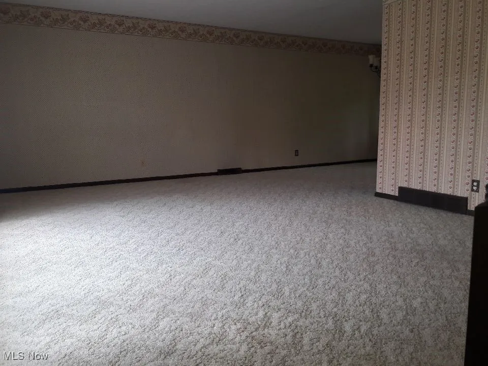 Carpeted empty room featuring wallpapered walls and baseboards