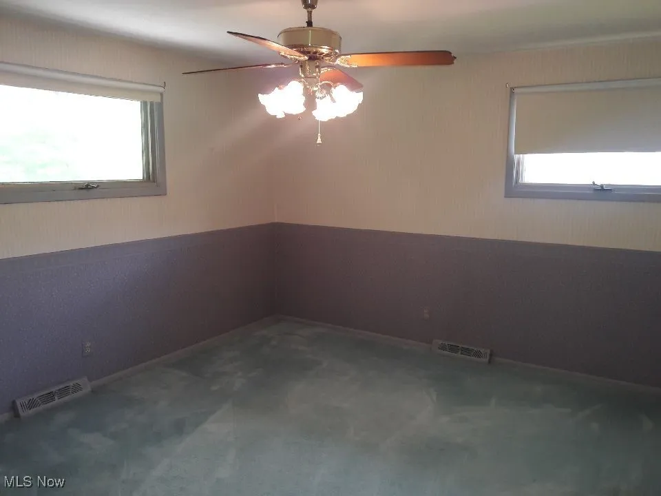 Unfurnished room featuring ceiling fan, a wainscoted wall, and carpet floors