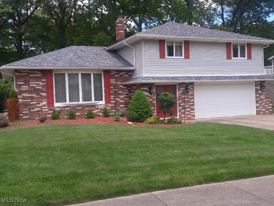 Split level home with a chimney, an attached garage, a front lawn, brick siding, and driveway