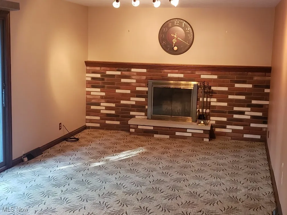 Unfurnished living room featuring carpet flooring and a glass covered fireplace