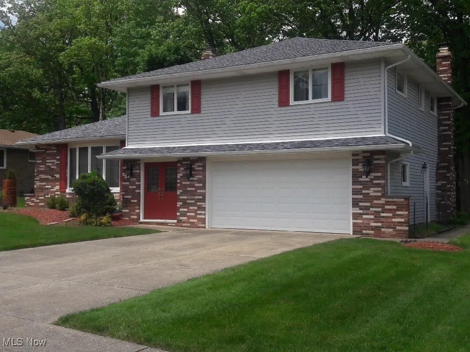 Split level home with brick siding, a chimney, driveway, a garage, and a front lawn