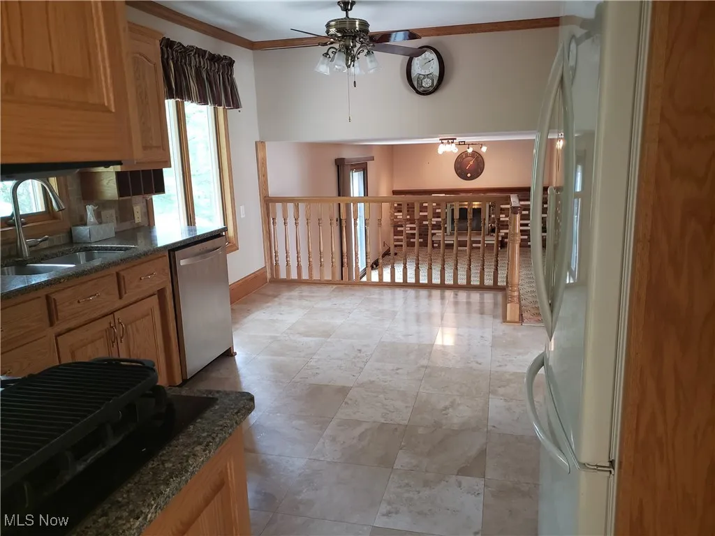 Kitchen featuring a ceiling fan, freestanding refrigerator, dishwasher, crown molding, and dark stone countertops