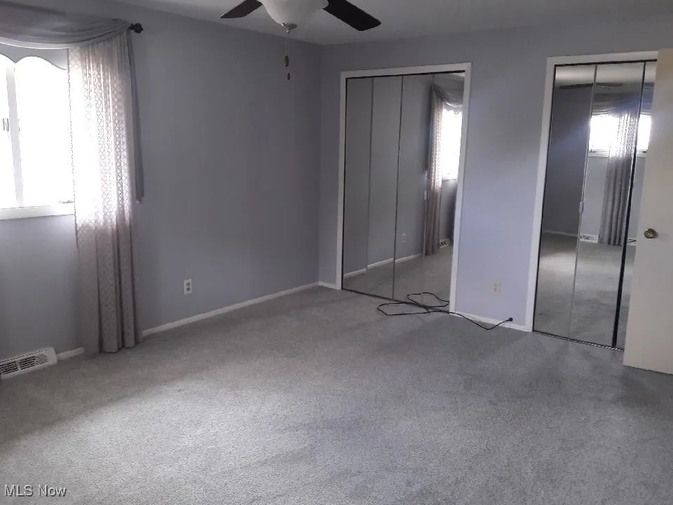 Unfurnished bedroom with two closets, multiple windows, carpet flooring, and a ceiling fan