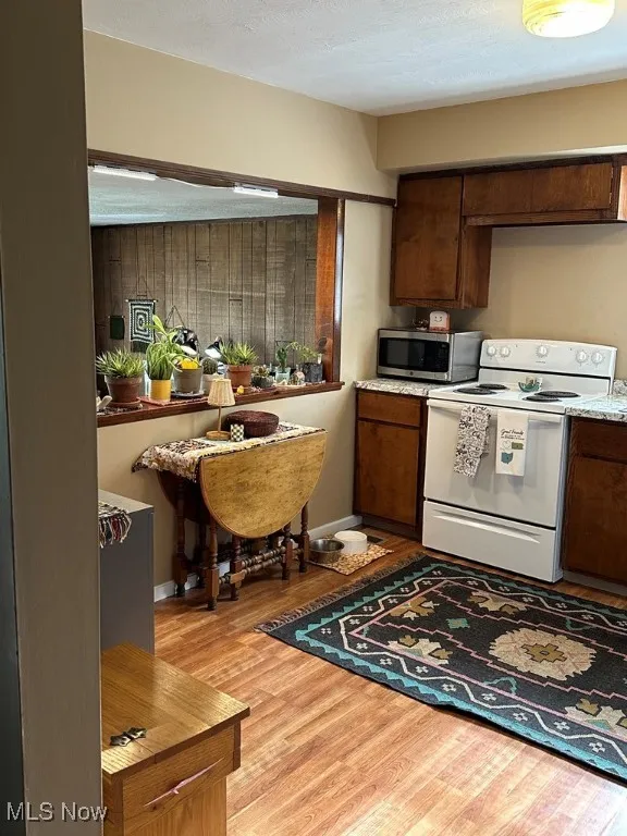 Kitchen with electric range, stainless steel microwave, light wood-type flooring, and light countertops