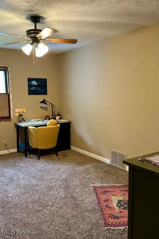 Carpeted home office with ceiling fan and a textured ceiling