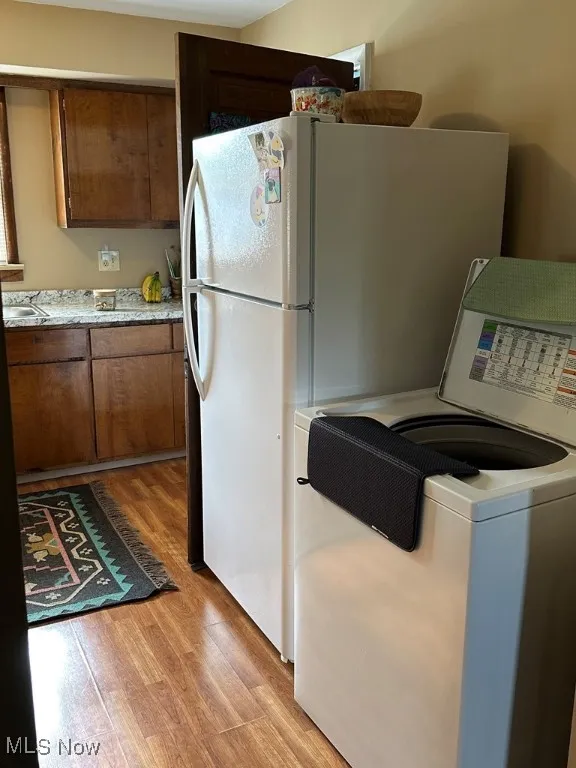Kitchen with washer / clothes dryer, light wood-style flooring, light countertops, freestanding refrigerator, and brown cabinetry