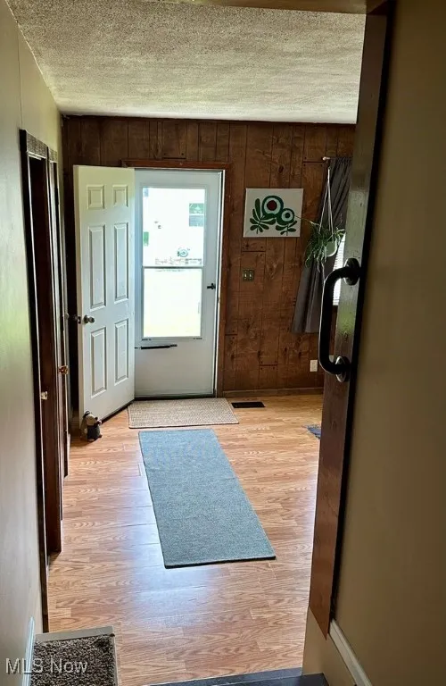 Foyer with light wood-type flooring, wood walls, and a textured ceiling