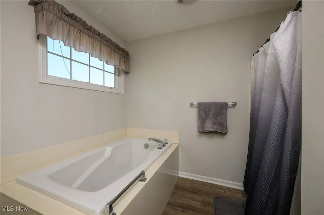 Full bathroom with wood finished floors, a garden tub, and a textured ceiling