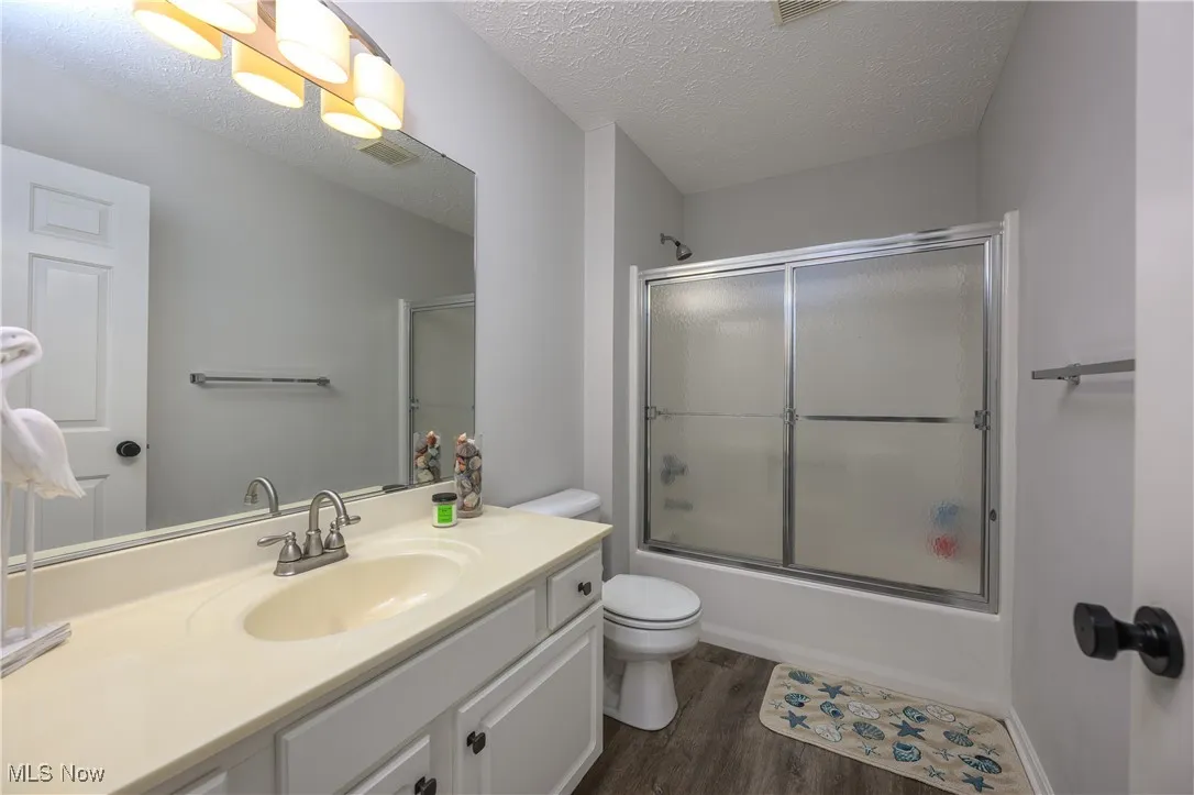 Bathroom featuring wood finished floors, vanity, bath / shower combo with glass door, and a textured ceiling