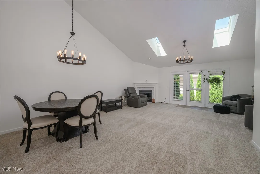 Carpeted dining space featuring a skylight, a chandelier, a tiled fireplace, and high vaulted ceiling