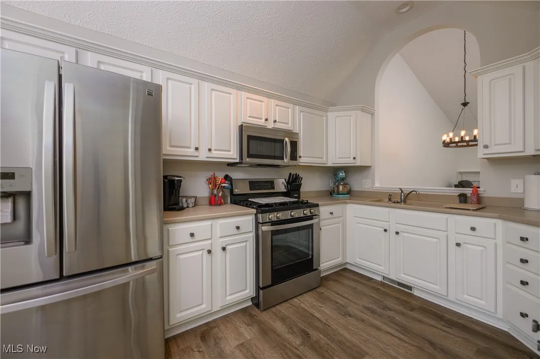 Kitchen with stainless steel appliances, vaulted ceiling, a chandelier, light countertops, and white cabinetry