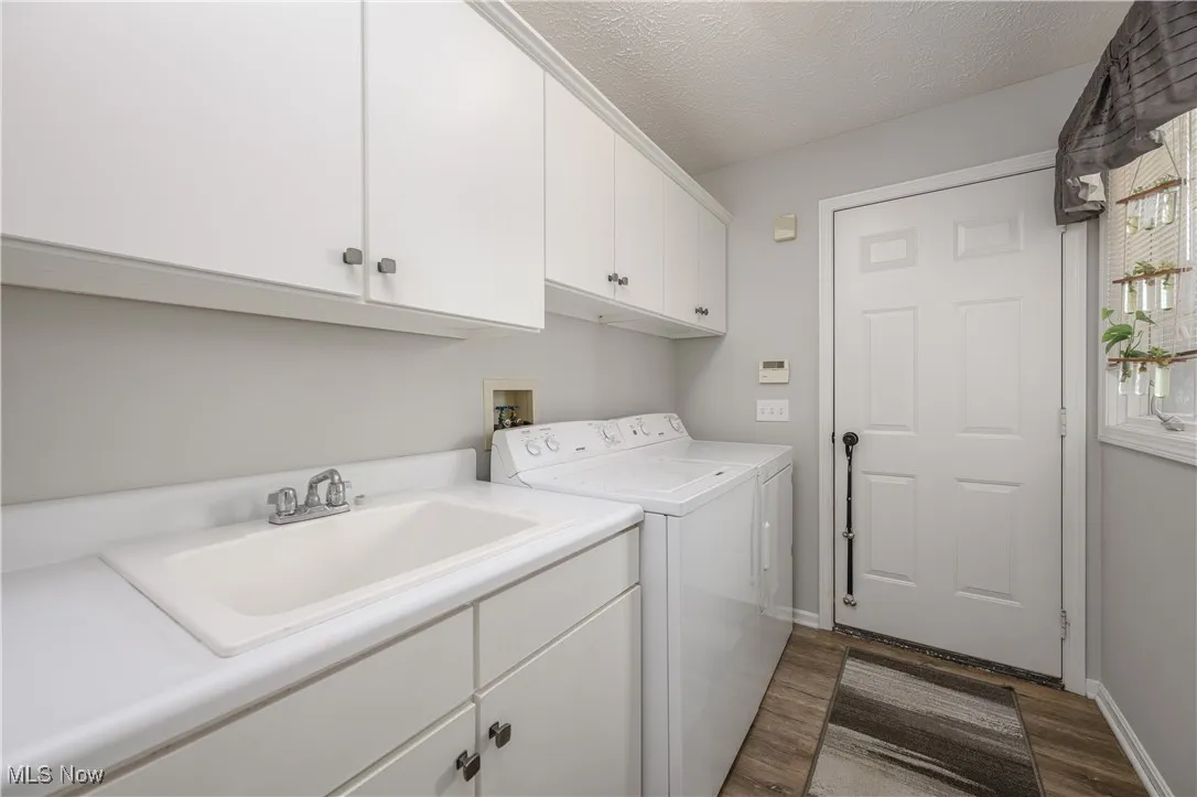 Laundry area with dark wood-type flooring, cabinet space, washer and dryer, and a textured ceiling