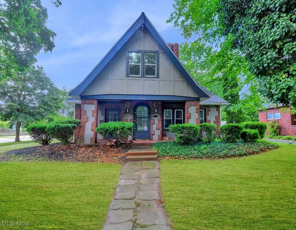 English style home featuring a chimney, brick siding, covered porch, and a front yard