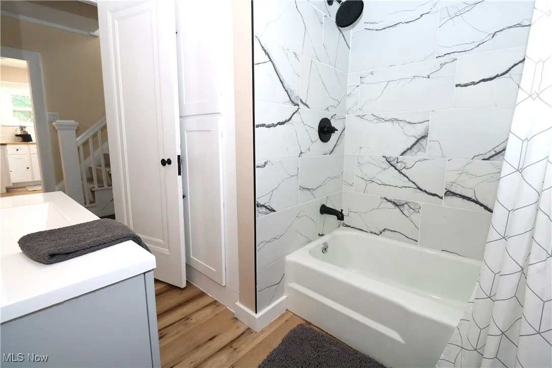 Bathroom featuring wood finished floors, shower / bath combination with curtain, and vanity