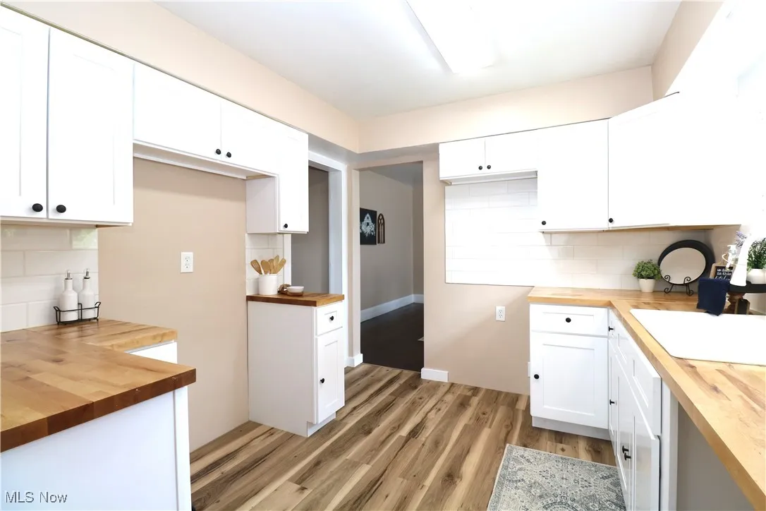 Kitchen with butcher block countertops, tasteful backsplash, light wood-type flooring, and white cabinets