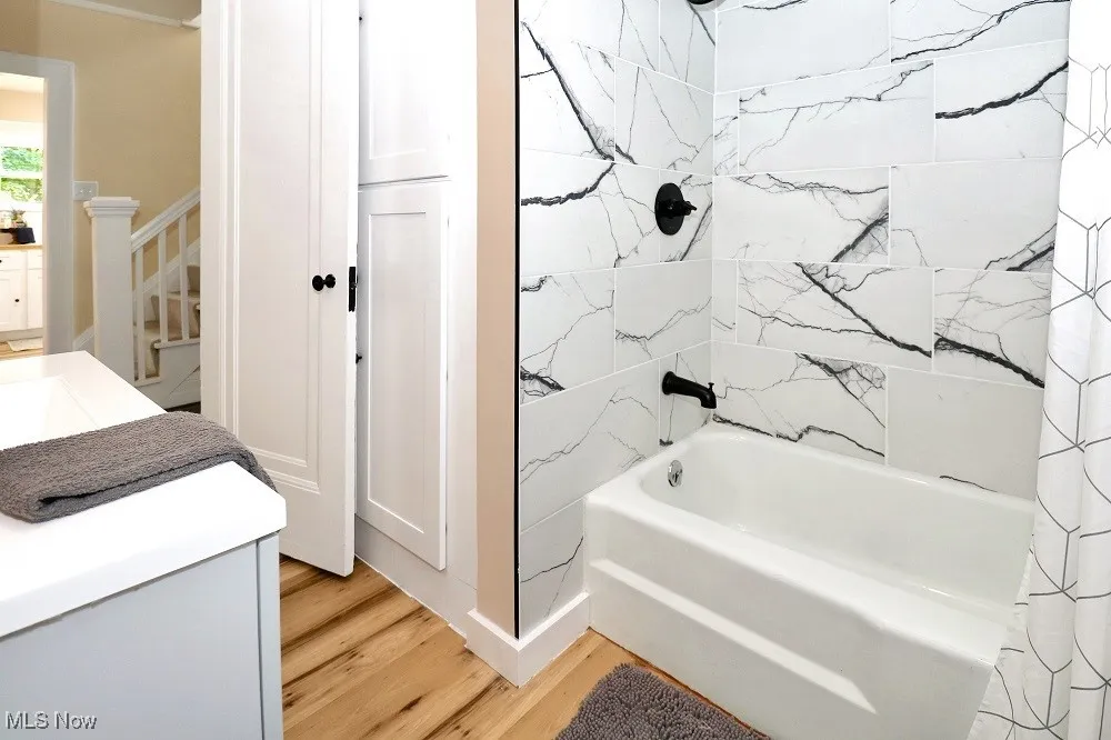 Bathroom featuring wood finished floors, shower / bath combo with shower curtain, and vanity