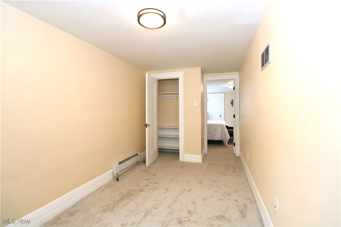 Unfurnished bedroom with baseboard heating, light colored carpet, and a closet