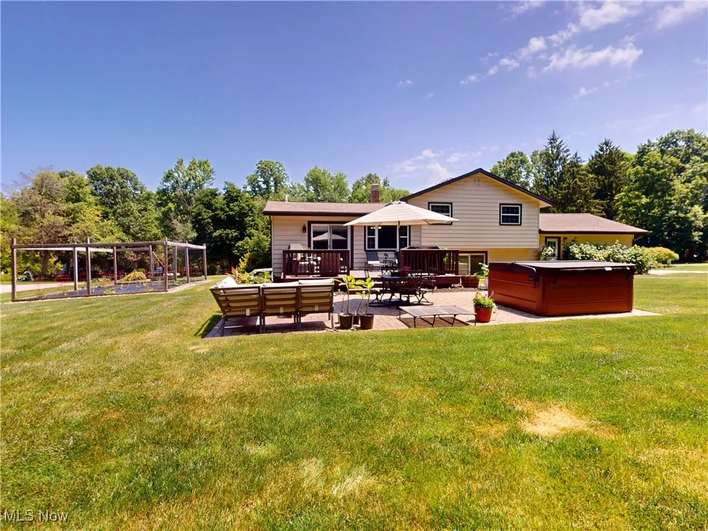 Back of property featuring a hot tub, a patio, a yard, outdoor lounge area, and a chimney