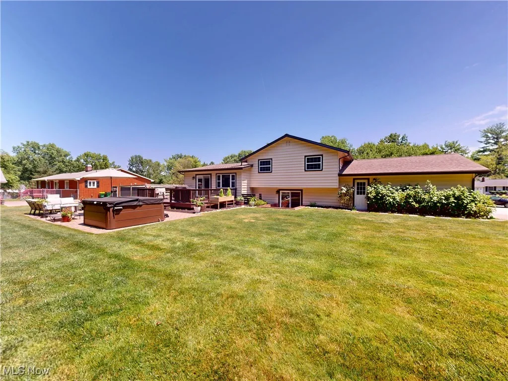 Back of house featuring a hot tub, a lawn, and a deck