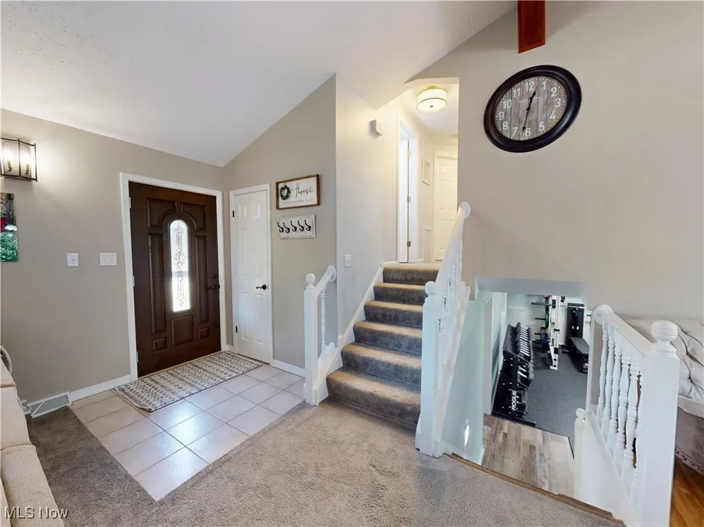 Carpeted entryway with vaulted ceiling, tile patterned floors, and stairway