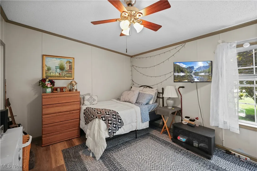 Bedroom with crown molding, lofted ceiling, wood finished floors, a ceiling fan, and a textured ceiling