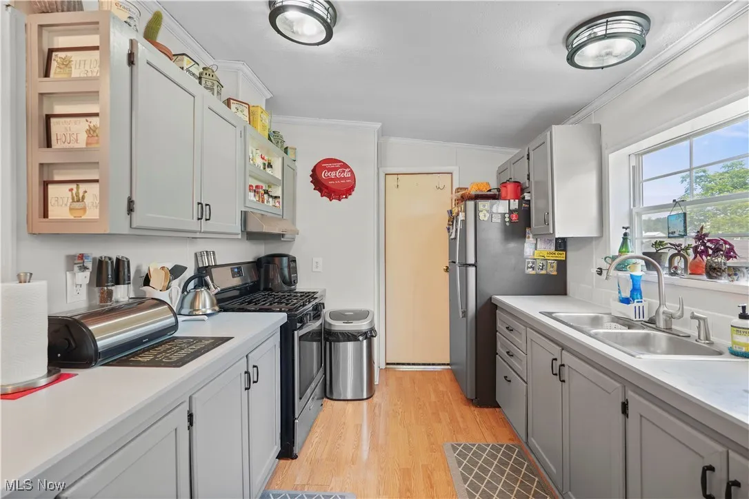 Kitchen featuring appliances with stainless steel finishes, crown molding, light wood-style floors, under cabinet range hood, and light countertops