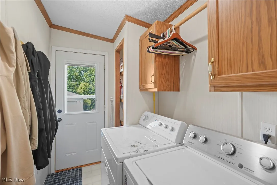 Washroom with washer and dryer, cabinet space, crown molding, and a textured ceiling