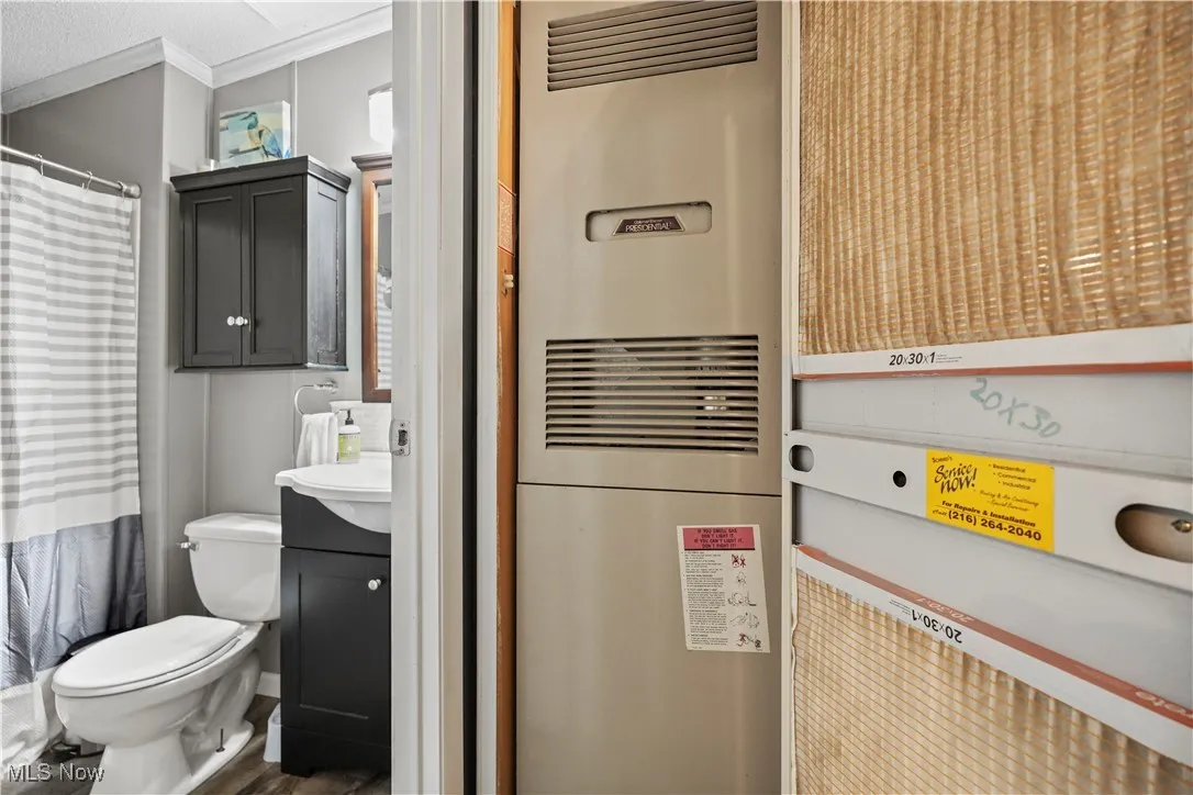 Full bathroom featuring a heating unit, vanity, ornamental molding, curtained shower, and wood finished floors