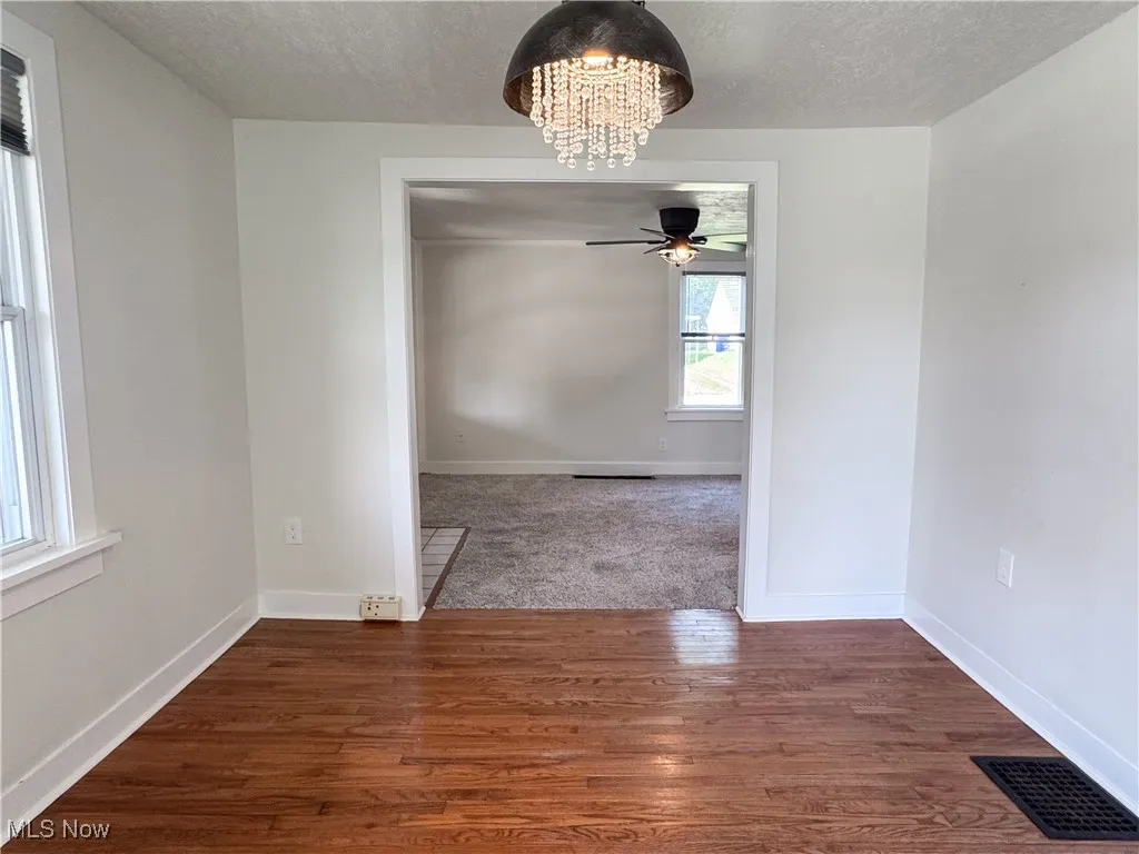 Unfurnished dining area featuring a chandelier, a textured ceiling, a ceiling fan, and wood  floors