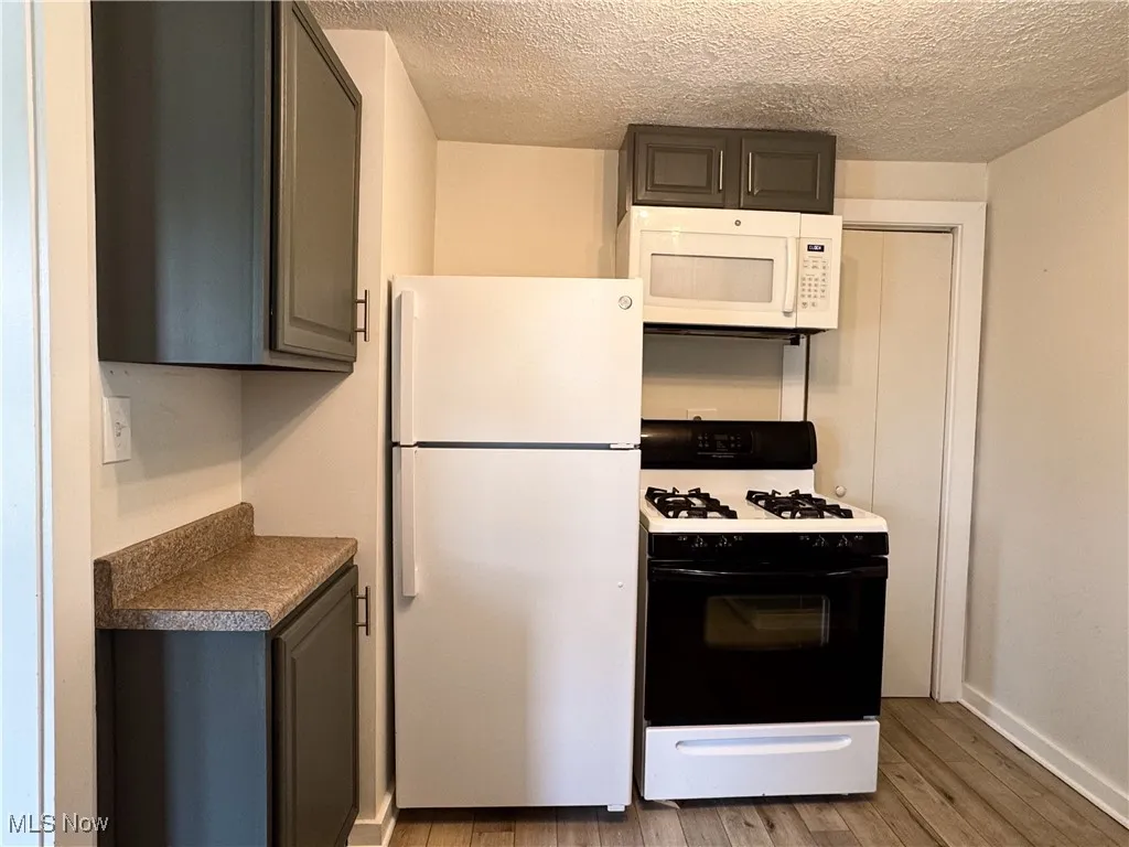 Kitchen featuring white appliances, light wood-type flooring, a textured ceiling, and gray cabinets