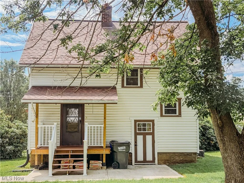 Rear view of house featuring roof with shingles, a chimney, and a lawn