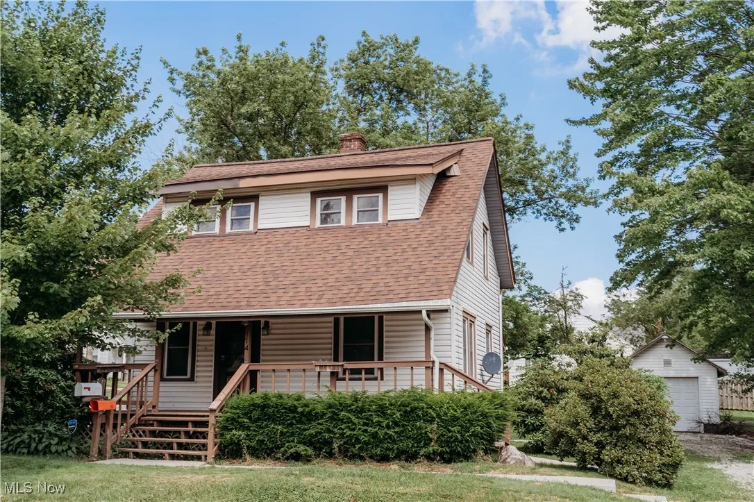 View of front of house featuring, a porch, a shingled roof, a chimney, and a garage