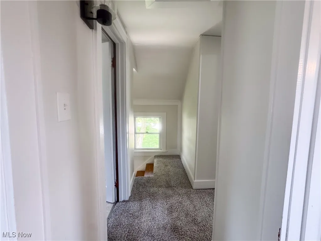 Hallway with carpet flooring and ornamental molding, and hall sconce