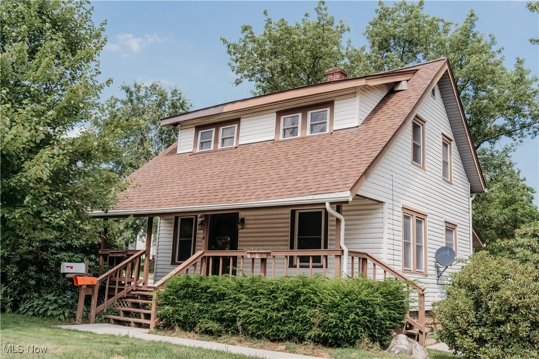 View of front facade with a shingled roof, a chimney, a porch, and stairway