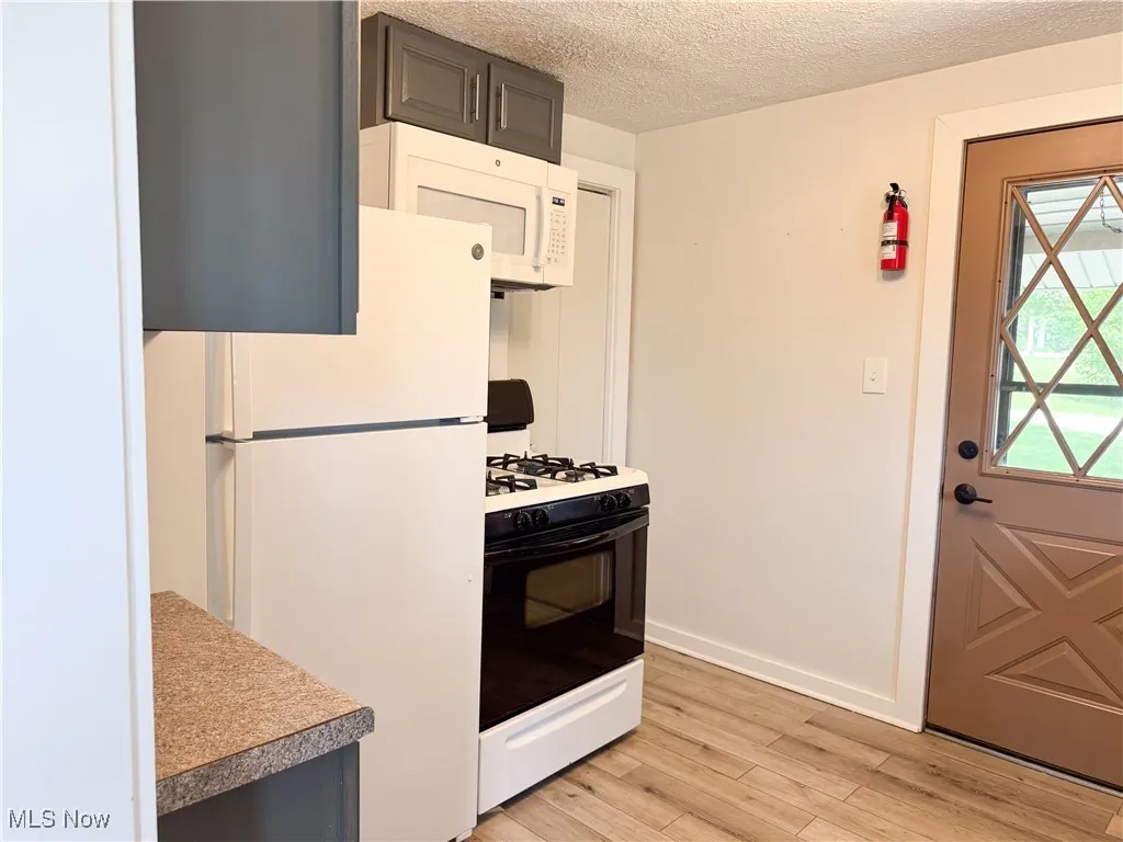 Kitchen with white appliances, light wood-style floors, a textured ceiling, and light countertops