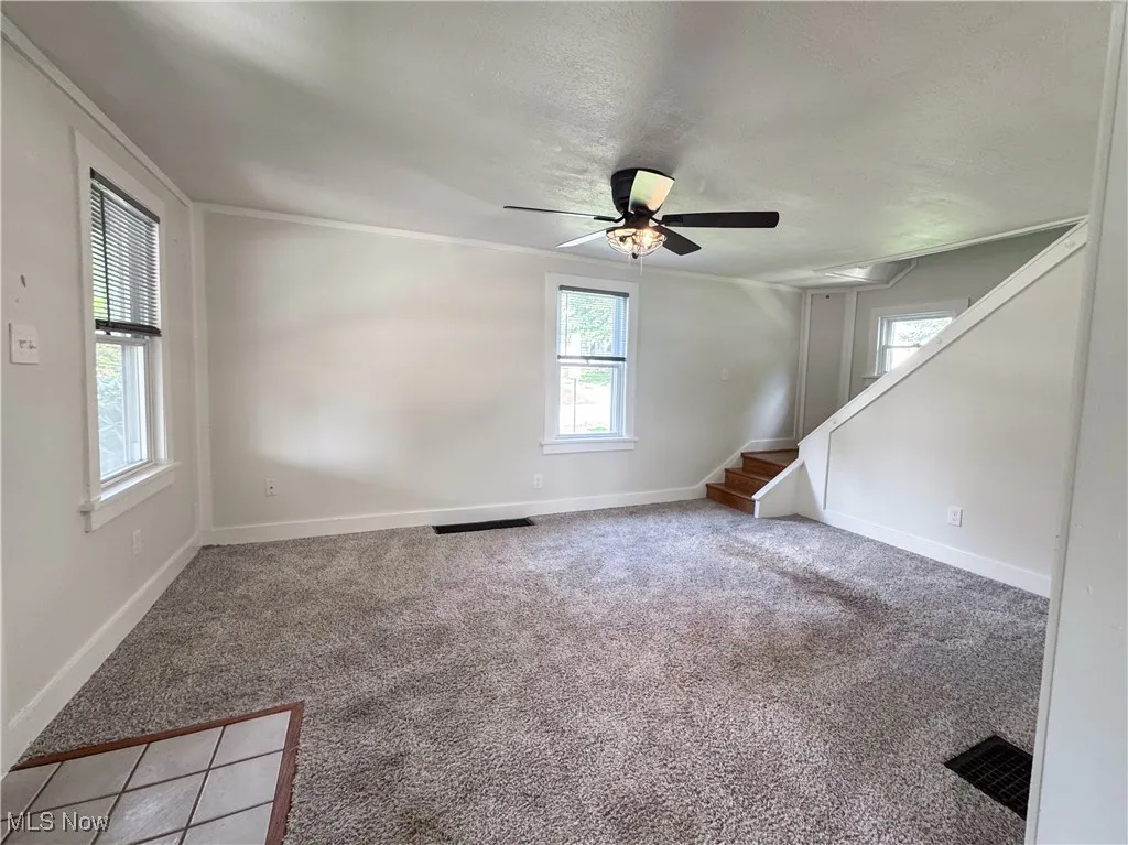 Living room featuring light colored carpet, stairway, a ceiling fan, crown molding, and a textured ceiling