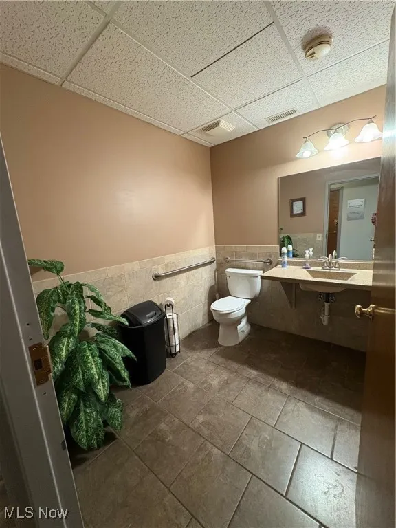 Bathroom with tile walls, a drop ceiling, and a wainscoted wall