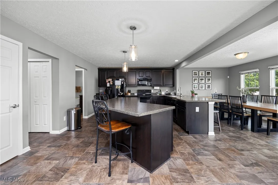 Kitchen with black appliances, breakfast bar, kitchen island, and a peninsula with another eating area view faces away from living