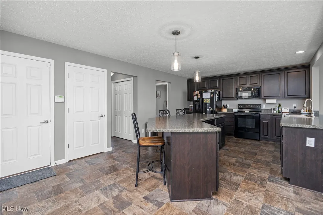 Kitchen with black appliances, breakfast bar, kitchen island, and a peninsula with another eating area view faces away from living