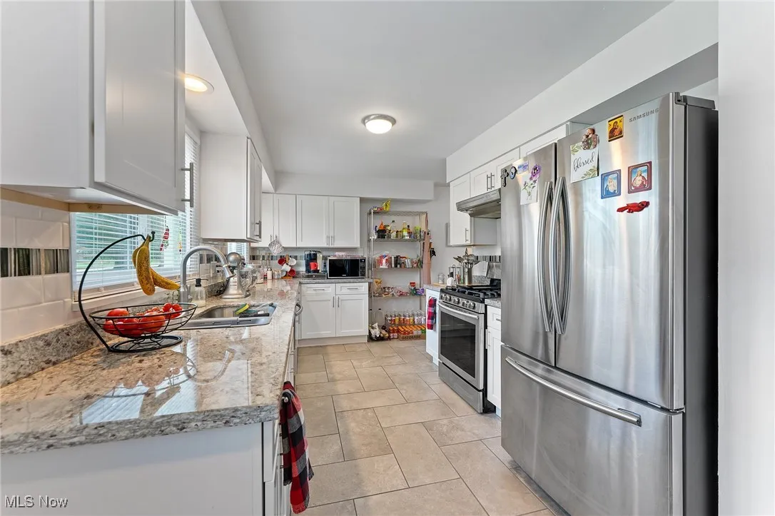 Kitchen featuring stainless steel appliances, white cabinets, under cabinet range hood, tasteful backsplash, and light stone counters