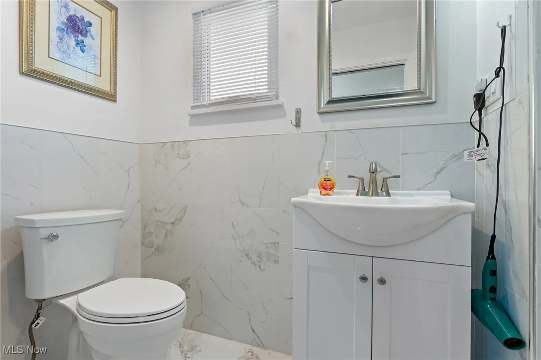 Bathroom featuring tile walls, vanity, marble finish floors, and wainscoting