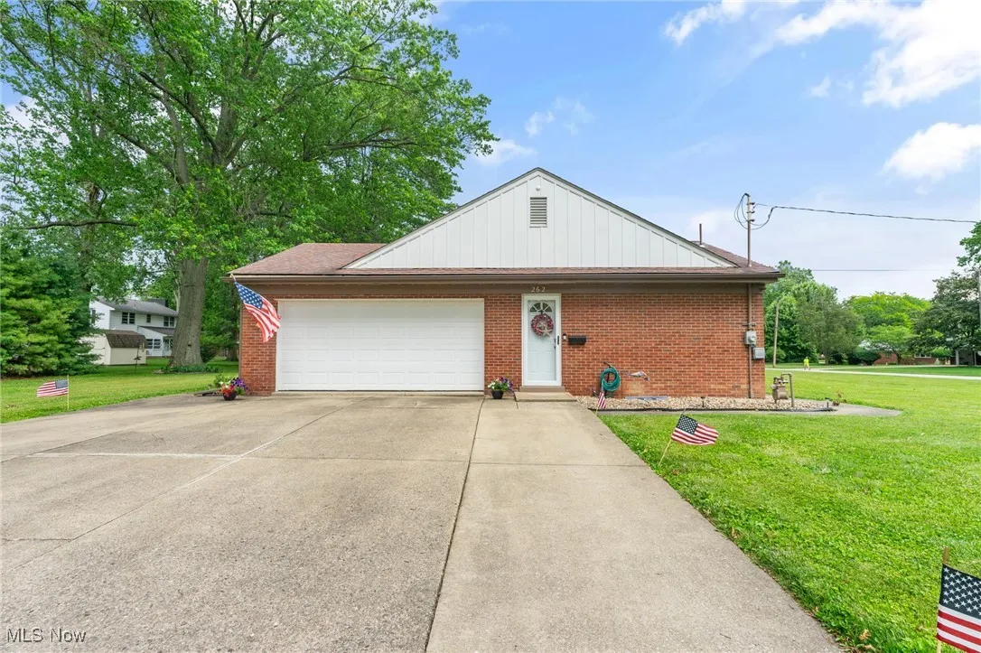 View of side of property featuring a front yard, driveway, brick siding, and a garage