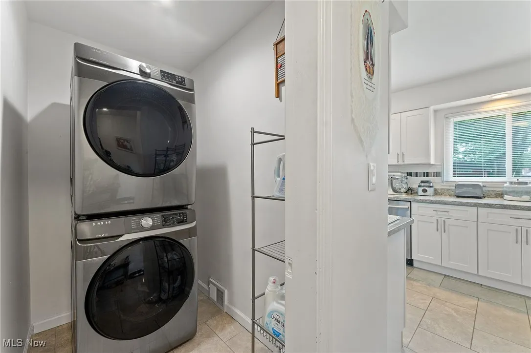 First Floor laundry room with stacked washer and dryer and light tile patterned floors.