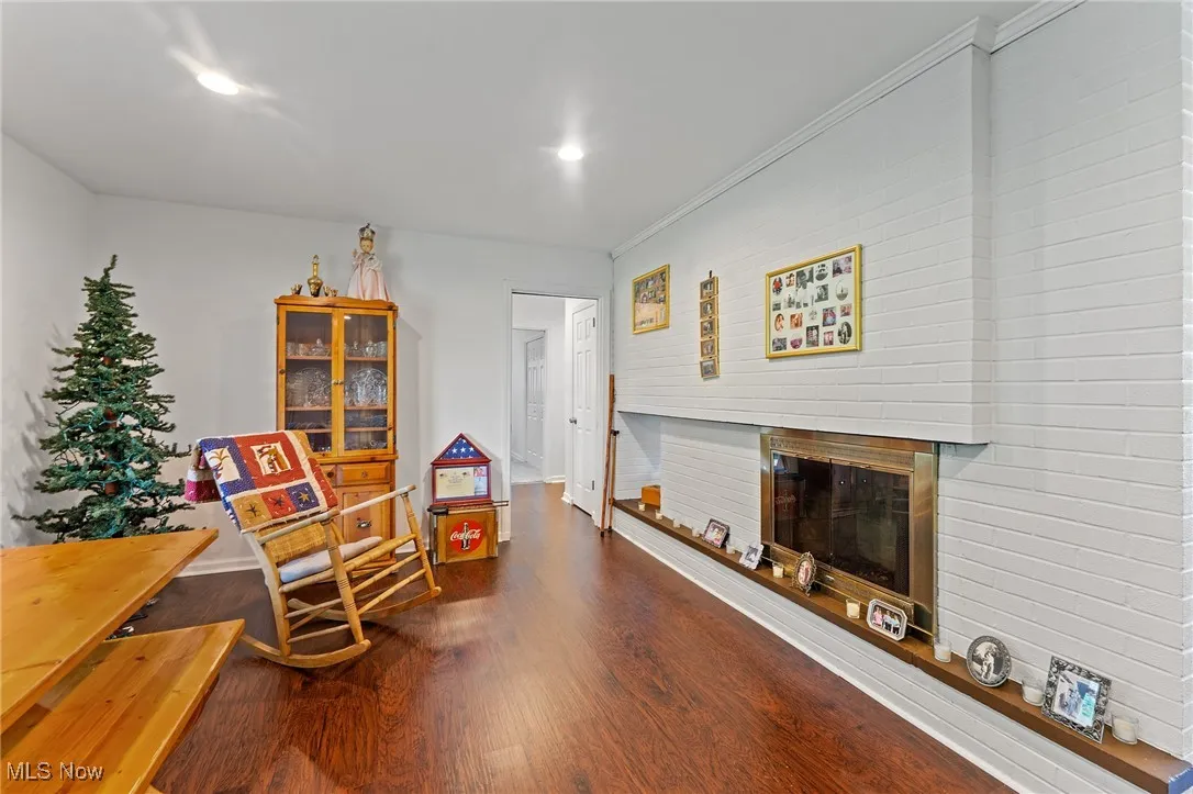 Living area with dark wood-type flooring, a glass covered fireplace, recessed lighting, and ornamental molding