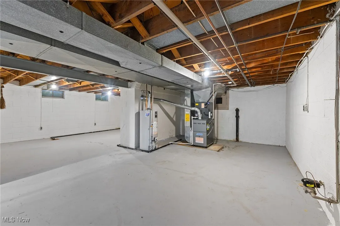 Unfinished basement featuring heating unit, gas water heater, and concrete block wall