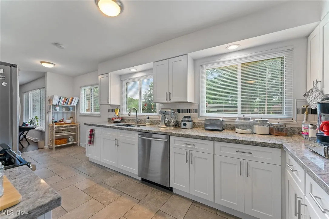 Kitchen with dishwasher, white cabinetry, and light stone counters