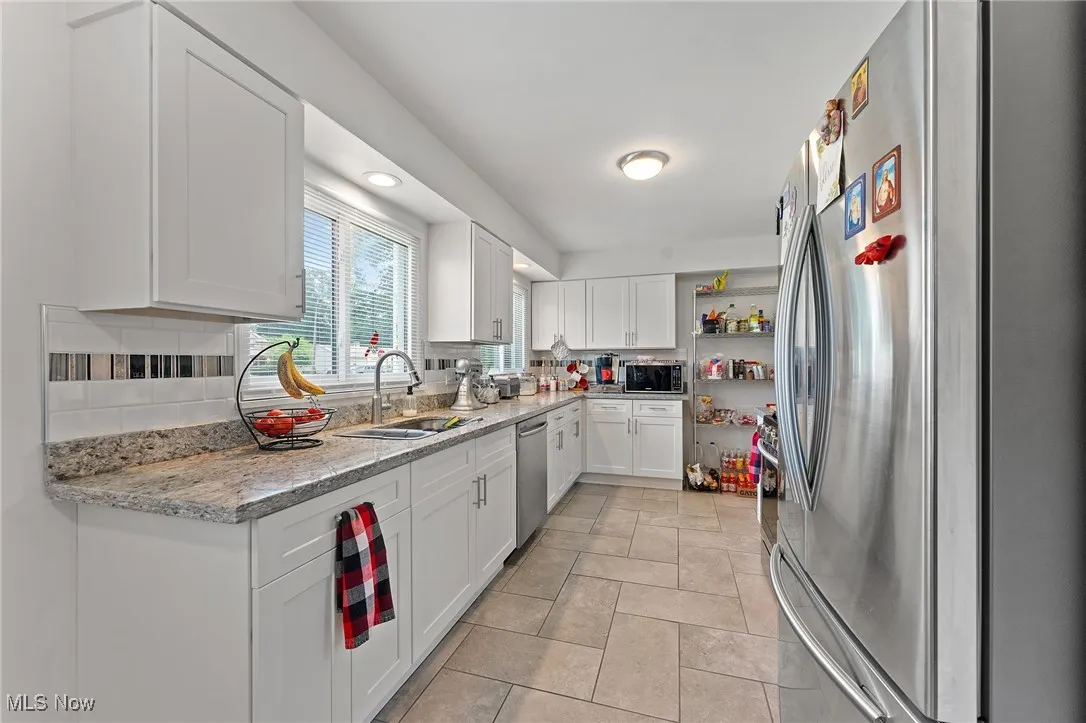 Kitchen with appliances with stainless steel finishes, tasteful backsplash, open shelves, and white cabinetry
