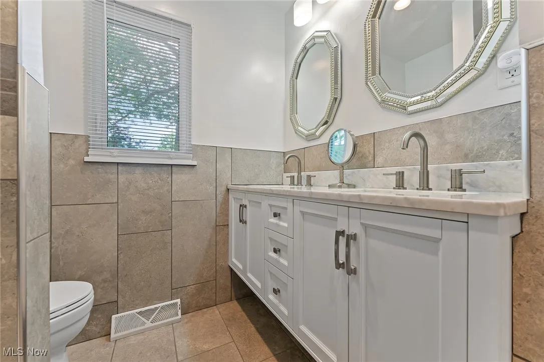 Full bathroom with tile walls, tile patterned flooring, double vanity, and a wainscoted wall